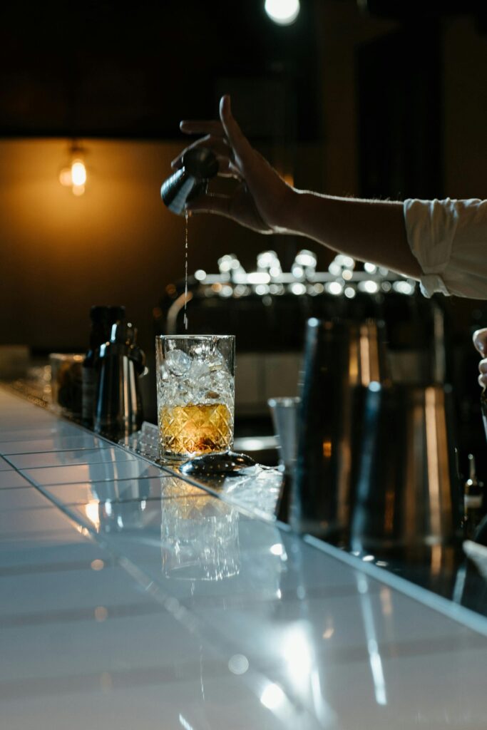 pexels-photo-4667032-4667032 Bartender skillfully pouring whiskey with ice in a dimly lit bar setting.